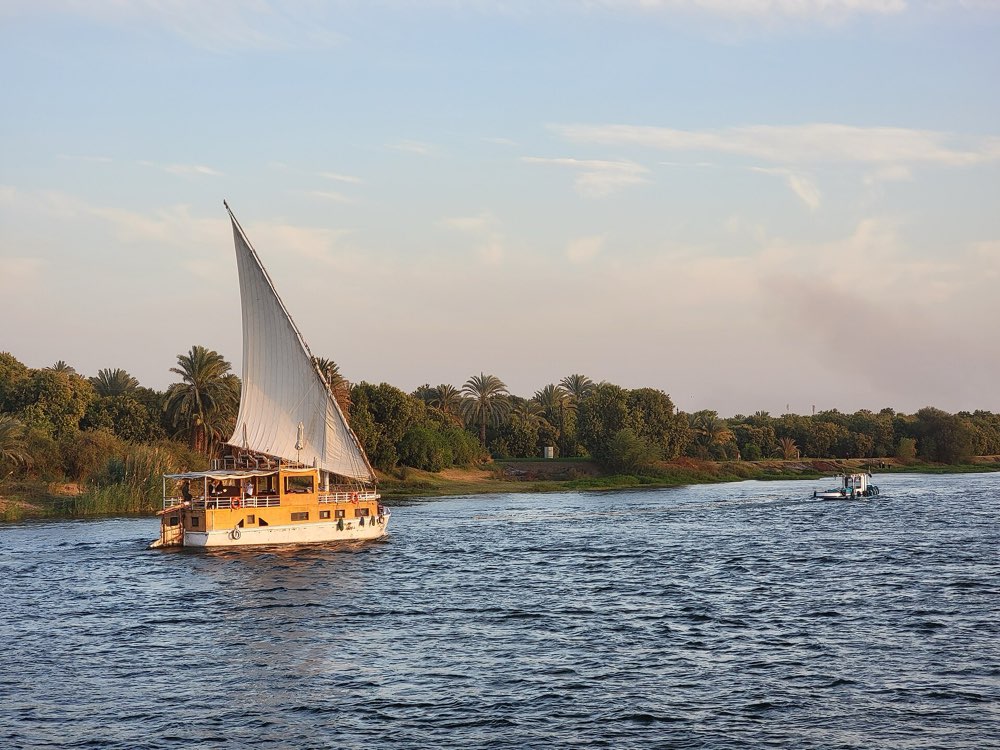 A wooden sailing boat with a large white lateen sail on the Nile in the evening light